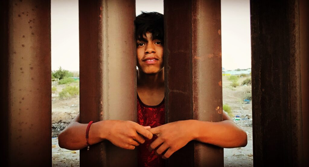 In Mexico, a young man threads his arms through the border wall.